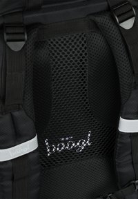 Interno dello zaino nero con un pannello posteriore in rete traspirante e un logo sottile. Le cinghie sono regolabili e dotate di dettagli in metallo resistenti.