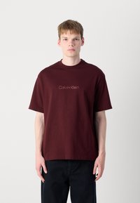 Burgundy cotton T-shirt with short sleeves and a crew neckline, featuring a subtle Calvin Klein logo in a lighter shade.