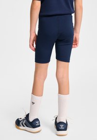 Marina blå sportshorts med en åtsittande design, tillverkade av stretchigt tyg. Kombinerade med vita ankelsockor och marina skor med en logotyp.