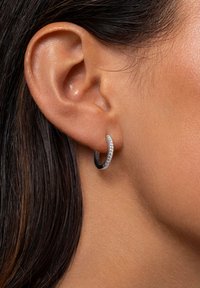 Pendiente de aro de plata con una elegante porción negra y una fila de pequeñas piedras transparentes que realzan su diseño moderno, llevado en la oreja de un modelo.