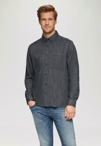 Marineblauwe geblokte button-up shirt met twee borstzakken, lange mouwen en blauwe knopen, gecombineerd met lichtblauwe jeans.