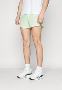 Ljusgröna sportshorts med nättextur, kortare än knäet, kombinerat med vita sneakers med gröna detaljer och vita strumpor.