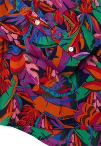 Camisa de algodón multicolor con un vibrante patrón floral en tonos de verde, rojo, púrpura y naranja; incluye botones blancos.