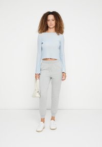 Ljusblå ribbad långärmad topp i kort längd, kombinerad med grå elastiska joggers och vita sneakers. Accessoarer inkluderar en liten vit väska.