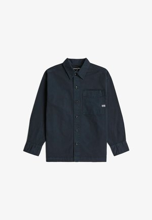 Chemise bleu foncé à manches longues, boutonnée, avec col et poche poitrine arborant une petite étiquette blanche sur le côté droit.