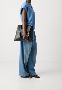 Sort læderhåndtaske med struktureret design og gul hardware. Båret med en blå chambray-top og oversized denimbukser.
