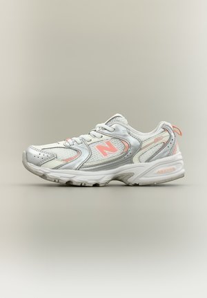 Chaussure de sport New Balance blanche et rose clair avec empiècements en mesh et synthétiques, lacets et semelle texturée, vue de côté sur fond neutre.