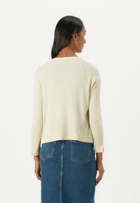 Pull en beige clair avec une texture côtelée, design court et manches longues. Associé à une jupe en denim avec des poches arrière.