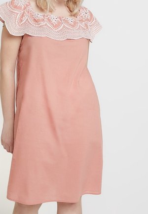 Robe en lin de couleur pêche avec un décolleté en lace blanche à bords festonnés. La robe est sans manches, avec une coupe décontractée et une longueur arrivant au genou.