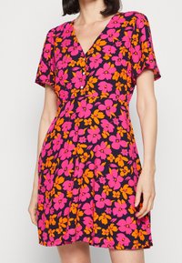 Kwiatowa sukienka w granatowym kolorze z żywymi różowymi i pomarańczowymi kwiatami. Krótkie rękawy, dekolt w kształcie litery V oraz detale z guzikami z przodu. Miękka tkanina.