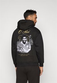 Crna dukserica s grafičkim printom nogometa�ša na leđima, uz natpise "O Rei" i "10" u zlatnoj boji. Mekana tkanina, opušteni kroj.