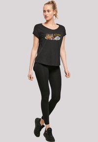 Svart bomullst-skjorte med "The Flintstones" grafikk, parret med svarte leggings og svarte joggesko. Enkel, casual stil.