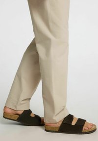 Svarta och bruna halkskor i sandalstil med urtagna mönster, korksula och texturerade remmar, parat med ljusbeiga tapered byxor.