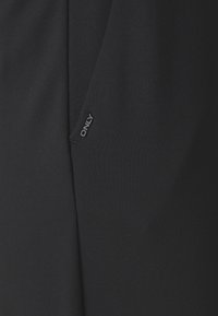 Černé kalhoty vyrobené z měkké tkaniny, s čistým designem a malou nášivkou "ONLY" na boku.