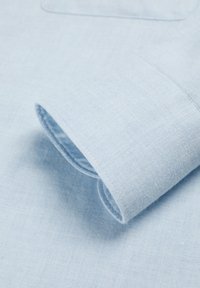 Cuello y puño de camisa de color azul claro con una textura suave y tejida; cuenta con un solo bolsillo en el pecho y un dobladillo bien terminado.