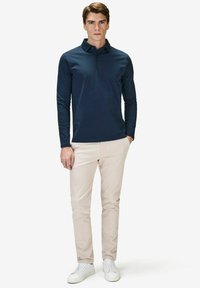 Marinblå långärmad polo med krage, kombinerad med ljusbeige byxor och vita sneakers, vilket ger en avslappnad stil.