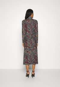 Robe longue ajustée couleur bourgogne foncé avec un motif floral. Comprend des manches longues, un col haut, et est associée à des talons noirs à lanières.