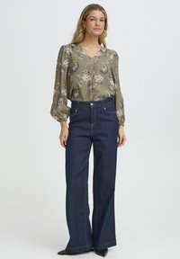 Õieprintidega teesärk oliivrohelises toonis, millel on V-kaelus ja paftvarrukad, kombineeritud kõrge vöökohaga tumedatest teksariidest laia säärega pükstega, millel on nähtavad õmblused.