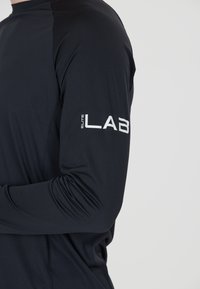 Zwart sportshirt met lange mouwen van textiel met een structuur. Voorzien van een wit "elite LAB" logo op de linkermouw. Strak sluitend ontwerp.