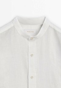 Weißes Leinenhemd mit Stehkragen, mit einer durchgehenden Knopfleiste und subtiler Textur. Das Etikett trägt die Aufschrift "Massimo Dutti."