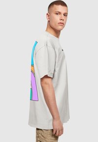 Hvid bomulds-T-shirt med en afslappet pasform, prydet med farverige abstrakte designs i blå, orange, pink og grøn på venstre side.