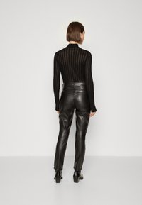 Un top negru cu mâneci lungi, cu dungi verticale și guler înalt, asortat cu pantaloni din piele neagră, cu talie înaltă, cu textură netedă și design ajustat.