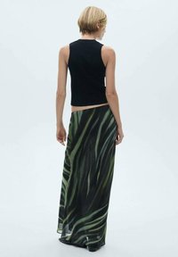 Zwarte geribbelde mouwloze top gecombineerd met een vloerlange groen en zwart patroon rok, lichte stof, losse fit.