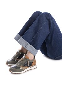 Zapatillas gris y marrón con un diseño texturizado, cordones en la parte delantera y cremallera lateral, combinadas con unos jeans azules oscuros arremangados.
