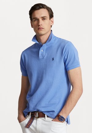 Polo de manga corta en azul claro con cuello y tapeta de dos botones. Presenta un pequeño logo bordado en el pecho y una tela texturizada.