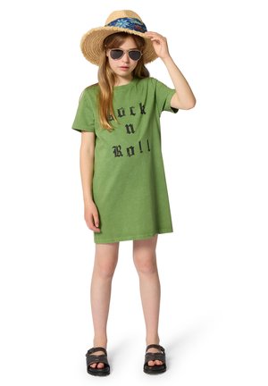 Robe t-shirt courte verte avec un motif noir "Rock n Roll", associée à un chapeau de paille et des lunettes de soleil. Des sandales plates complètent le look.