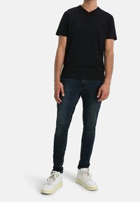 Camiseta negra de algodón de manga corta y escote en V combinada con jeans azules ajustados y zapatillas altas blancas.