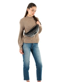 Riñonera negra y gris hecha de lona, con una cremallera lisa y un parche rectangular. Llevada por un modelo con un suéter beige y vaqueros azules.