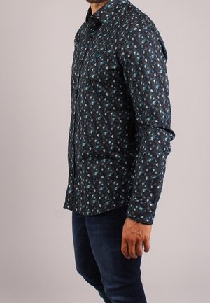 Chemise cintrée à manches longues de couleur bleu foncé avec un motif floral en bleu clair et blanc. Elle possède un col classique.