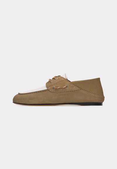 Mocassin en suède marron clair et beige avec détail en lacet et semelle plate noire, vue de côté sur fond blanc uni.