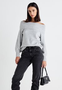 Gray off-the-shoulder sweater with ribbed neckline and cuffs, paired with high-waisted black jeans and a small black handbag.