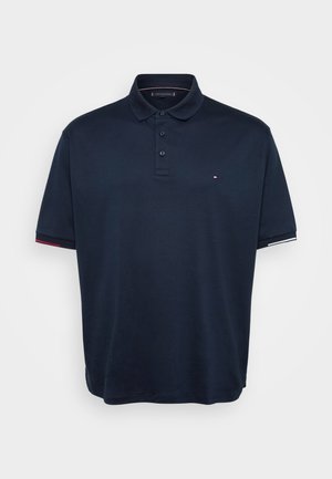 Mørkeblå polo skjorte laget av bomull, med klassisk krage, tre knapper og kontrasterende røde og hvite detaljer på ermene.