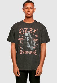 Tricou negru din bumbac, oversized, cu un imprimeu grafic care prezintă un bărbat cu păr lung și ochelari de soare, textul spune "OZZY" și "OSBOURNE" în roz.