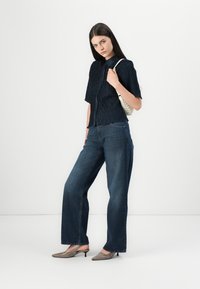 Donkerblauwe gekreukte overhemd met knopen, gecombineerd met wijde blauwe jeans en grijze puntige hakken. Accessoire: kleine lichtgekleurde handtas.