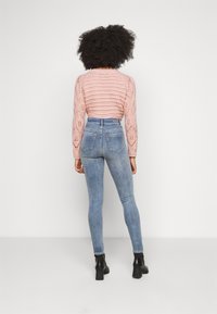 Suéter de punto rosa claro con rayas texturizadas y detalles de encaje, combinado con jeans skinny de cintura alta azul claro y botas de tacón negras.
