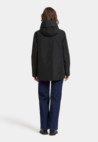 Svart, vattentät jacka med hög krage och justerbar huva, med en slät textur. I kombination med mörkblå utsvängda jeans och svarta skor.