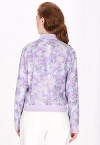 Bloemen bomberjack van lichtgewicht stof, met een pastelpaarse achtergrond en roze en blauwe bloemen. Geribbelde manchetten en zoom.