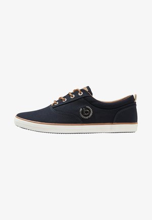 Zapatillas de lona navy con ojales y detalles en marrón, que presentan un logo circular en el lateral y una suela de goma blanca. Diseño ligero y de corte bajo.