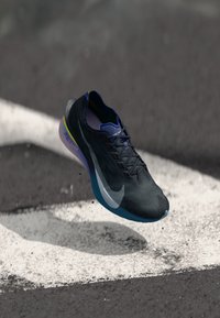 Svart løpesko med teksturert overdel, blå såle og grønne detaljer. Har et dynamisk design og en fremtredende hvit Nike-logo på siden.
