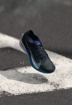 Svart løpesko med teksturert overdel, blå såle og grønne detaljer. Har et dynamisk design og en fremtredende hvit Nike-logo på siden.