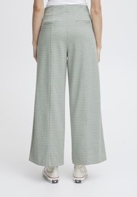 Pantalons larges à motif à carreaux vert clair, avec une taille haute, deux poches arrières, et associés à des baskets blanches.