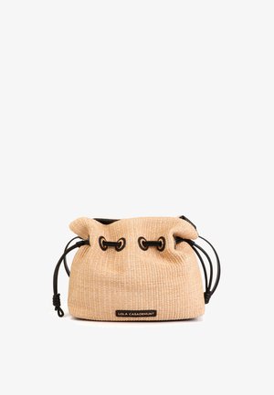 Bolsa con cordón de fibra natural en beige con herrajes negros, superficie texturizada y etiqueta con logo. Cuenta con asas de cuerda ajustables para mayor versatilidad.