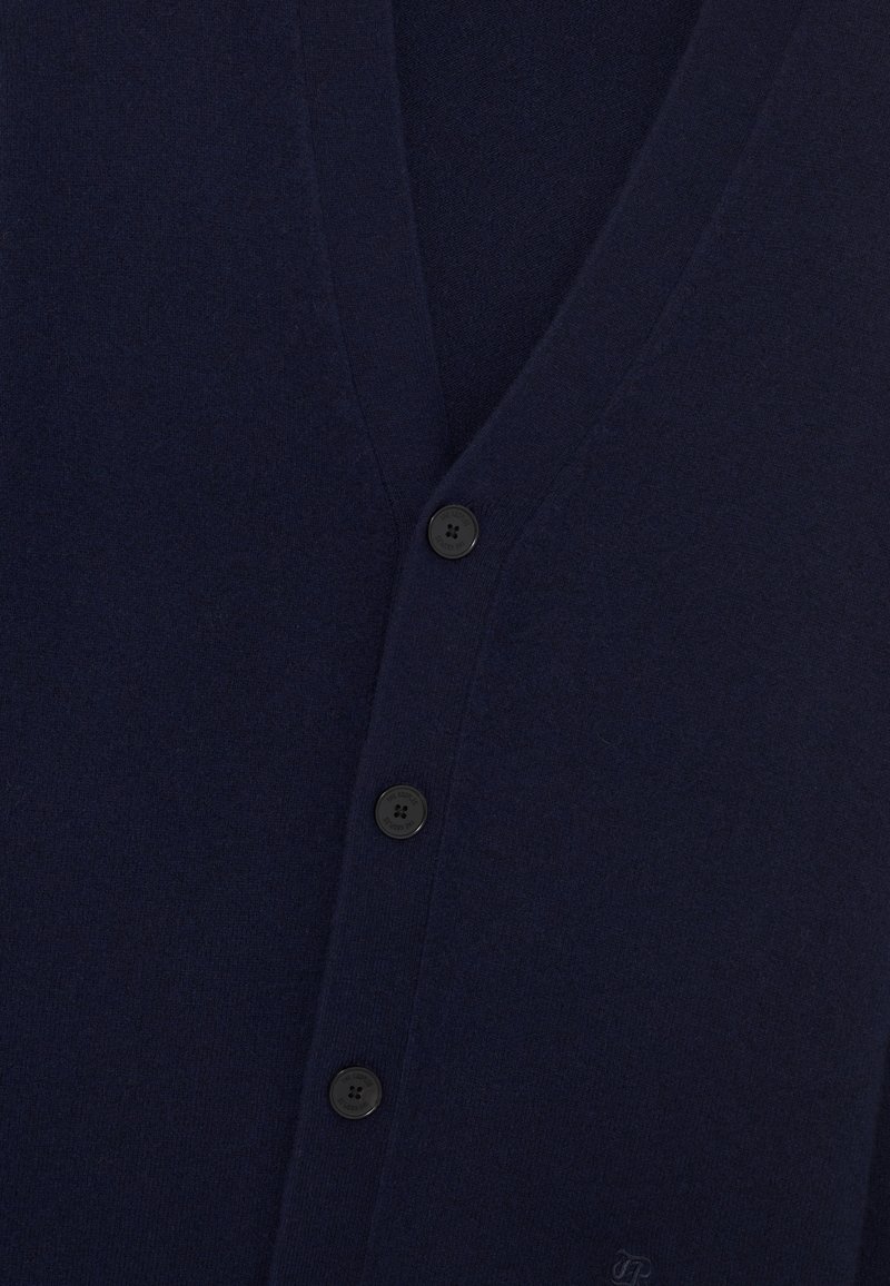 Navy blue cardigan made of soft wool, featuring a V-neck, six black buttons, and a textured surface with a logo on the bottom.