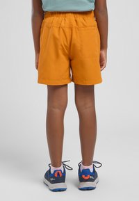 Orange Shorts mit einem elastischen Bund, glatter Textur und Gesäßtasche. Kombiniert mit blauen und grauen Sport Schuhen.