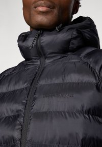 Giubbotto impermeabile nero con colletto alto, caratterizzato da sezioni trapuntate e una cerniera. Ricamo del logo sul petto. Materiale strutturato e leggero.