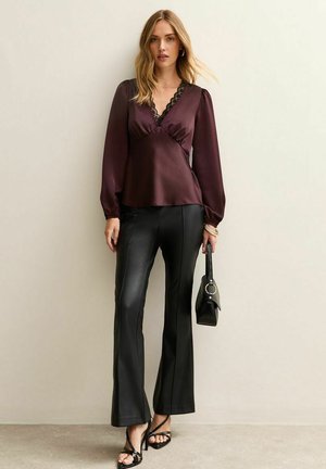 Bordeaux satijnen blouse met kantafwerking, lange mouwen en een V-hals, gecombineerd met zwarte neplederen uitlopende broek en een minimalistische zwarte handtas.